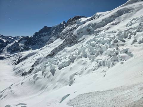 Expansive snowy alpine slope with jagged ice formations beneath towering peaks.