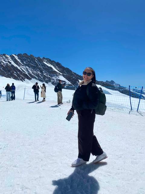 Woman standing on a snowy plateau with other tourists and a mountain ridge behind.