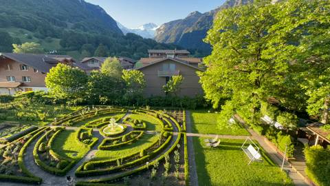 Manicured garden maze in a village with snow-covered alpine peaks rising in the distance.
