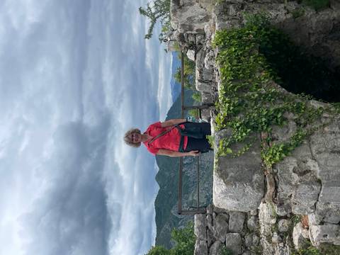 Smiling traveller stands on ivy-covered stone ruins with mountain backdrop.