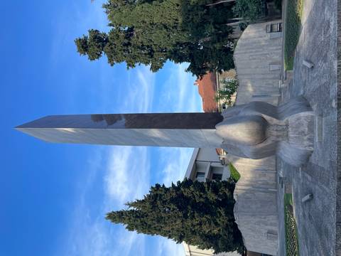 Modern stone obelisk emerging from sculpted hands in a small park.