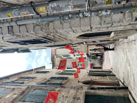Narrow stone lane in Kotor lined with hanging Montenegrin flags and small shops.