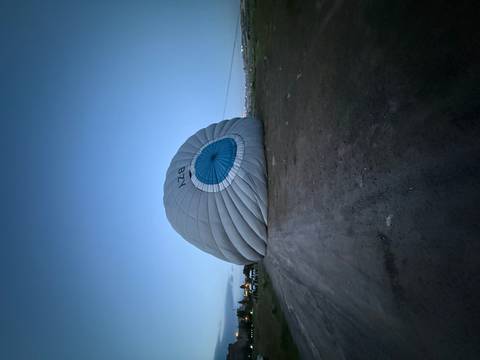 Deflated hot air balloon envelope lying on an open field in early dawn light.
