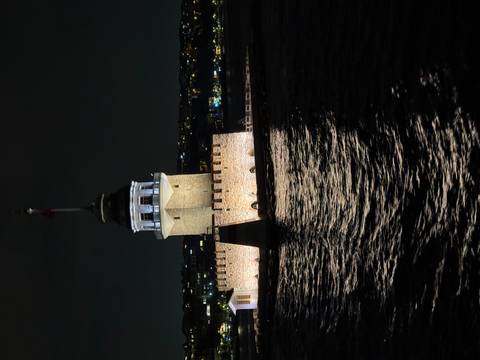 Istanbul’s Maiden’s Tower illuminated at night reflecting off dark Bosphorus waters.