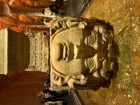 Upside-down Medusa head column base in the dimly lit Basilica Cistern surrounded by coins.