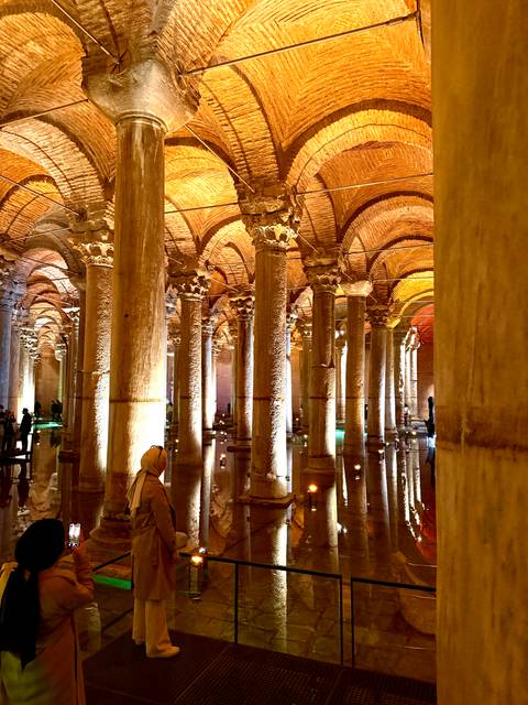 Illuminated rows of ancient stone columns reflecting in shallow water inside a historic underground cistern.