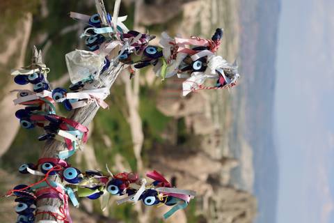 Tree branch adorned with colorful ribbons and blue Nazar amulets against blurred rock formations of Cappadocia.