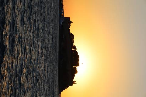Silhouetted island fortress against a vivid orange sunset over gently rippling sea.