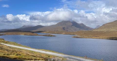 Quiet loch with rolling moorland and a cloud-capped mountain ridge reflected in calm water.