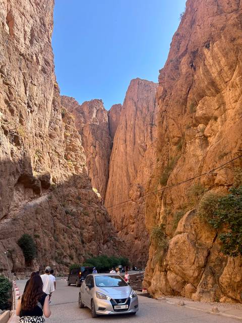Steep red-rock walls of Todra Gorge rising toward blue sky with narrow trail.