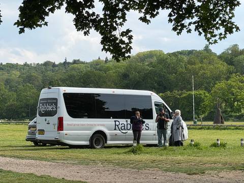 Rabbie's tour minibus parked in a green meadow with three travellers chatting beside it.
