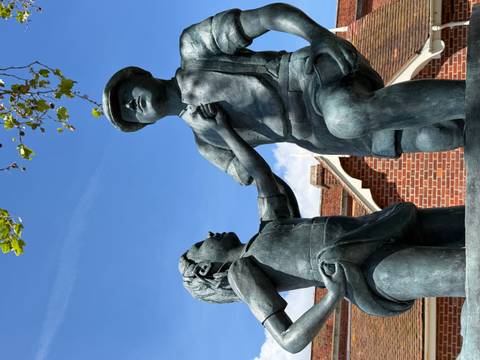 Bronze statue of two children outside a red-brick building under blue sky.