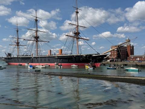Historic ironclad warship HMS Warrior moored in a harbour with small boats and reflections.