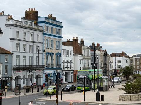 Lively seaside street lined with colourful Victorian buildings, buses, cars and pedestrians.