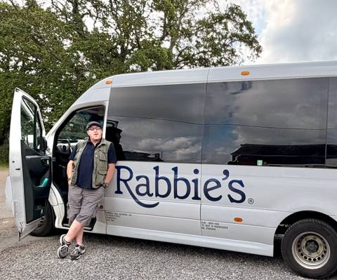 Tour driver leaning against a Rabbie's minibus door in a rural setting.
