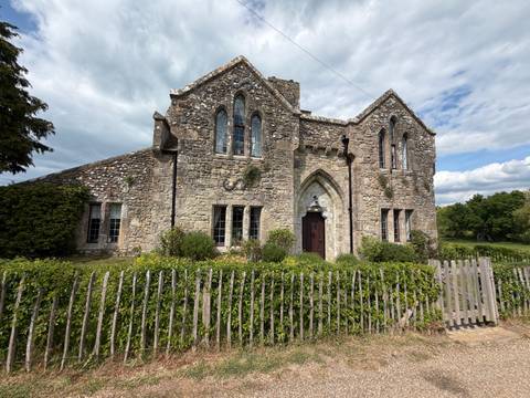 Historic stone building with Gothic windows and arched doorway in rural setting.