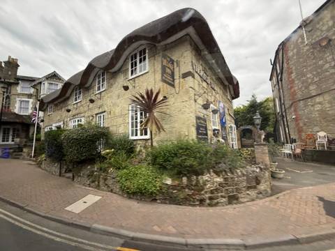 Motion-blurred street view of a rustic cottage with wavy roof captured from a moving vehicle.