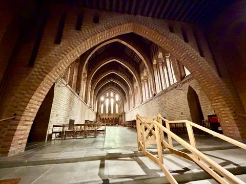 Vaulted brick interior of an abbey or church hall with dramatic arches and pews.