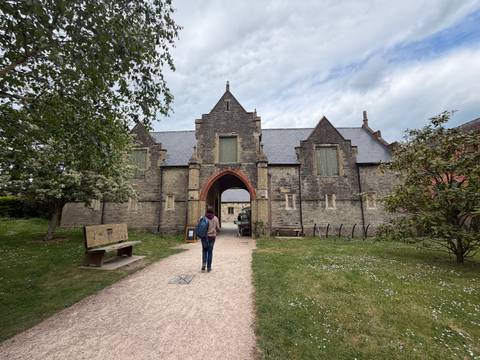 Visitor walking toward a stone abbey entrance with arched gateway and grassy courtyard.