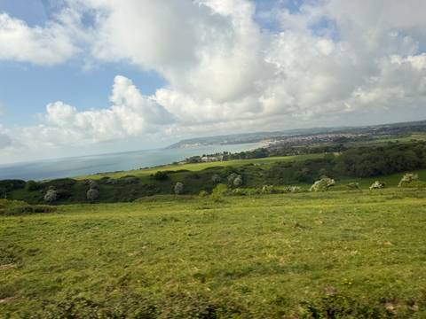 Sweeping coastal panorama of green fields leading to cliffs and the sea under scattered clouds.