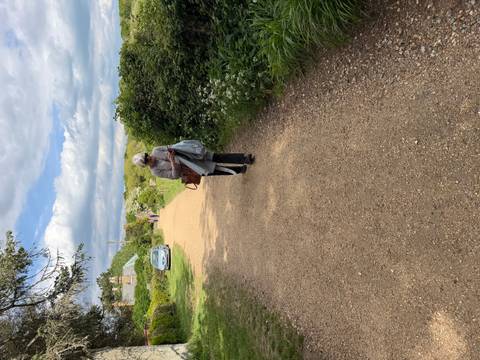 Woman walking down a gravel country path with hedgerows and distant cottages.