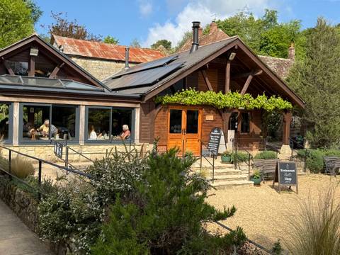 Rustic timber restaurant building with solar panels and diners visible through large windows.