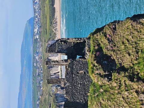 Clifftop ruins of Dunluce Castle overlooking turquoise sea and distant Causeway Coast.