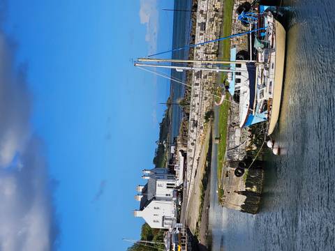 Small harbor with sailboat moored beside stone quay under bright blue Irish sky.