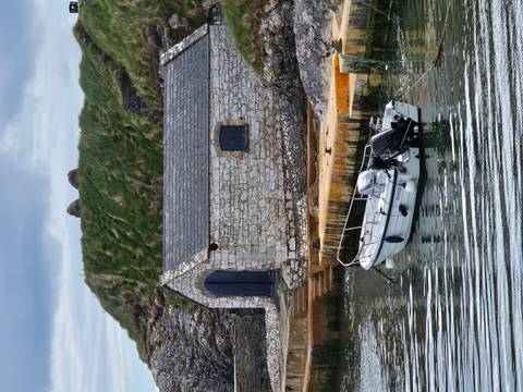 Quiet stone boathouse and small dinghy on reflective inlet with grassy mound.