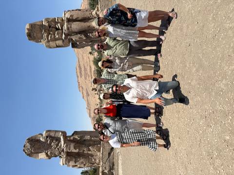 Group posing in front of Colossi of Memnon with desert hills in background.