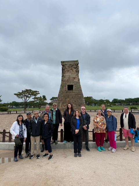 Tour group poses before Cheomseongdae stone observatory under an overcast sky in Gyeongju.