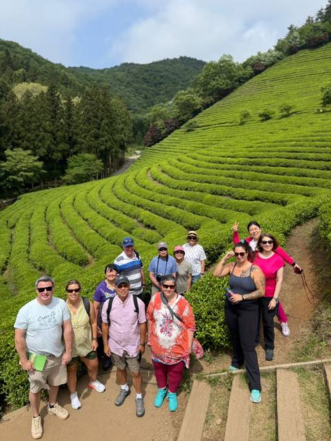 Smiling visitors stand among bright green rows of a terraced tea plantation.