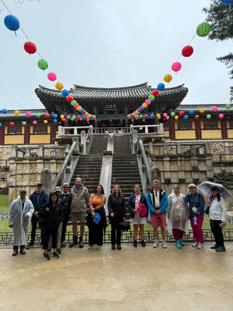 Travelers stand on the grand stone staircase of a colorful lantern-decorated Buddhist temple after rain.