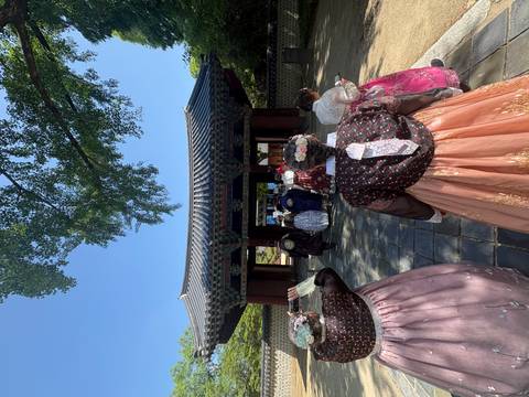 Tourists in vibrant hanbok walk toward an ornate palace gate along a tiled courtyard.