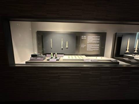 Glass museum case displaying ancient bronze daggers and small green artifacts with explanation panels.