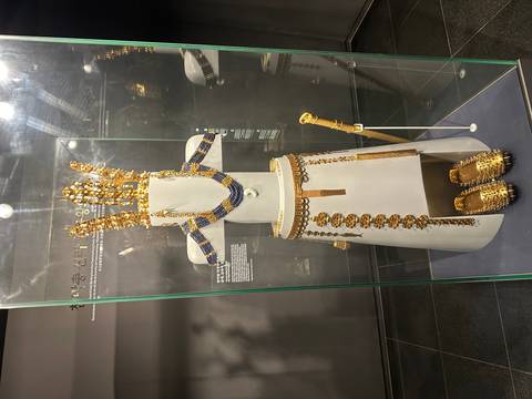 Full ceremonial gold regalia reconstructed on a white mannequin inside a glass museum case.