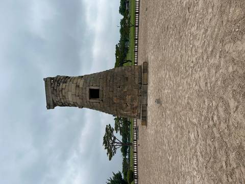 Stone Cheomseongdae astronomical observatory standing alone on a gravel yard under a gray sky.