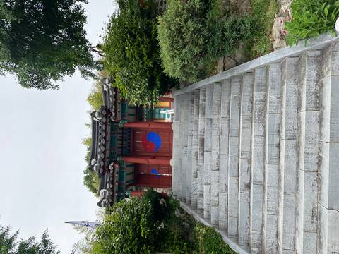 Stone stairway leading to a traditional Korean gate painted red with blue yin-yang symbols surrounded by trees.