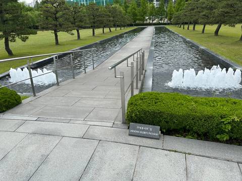 Granite walkway over a shallow reflecting pool with fountains and a plaque labelled 'Unknown Soldiers Walkway'.