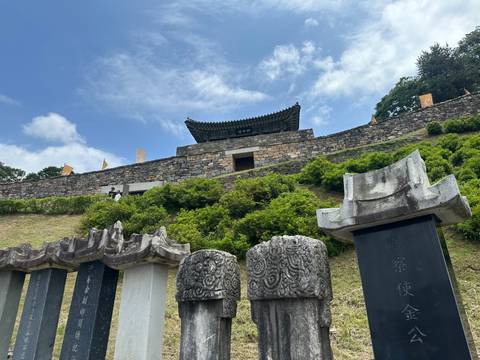 Stone fortress wall and gate on a hilltop under blue sky with carved stone tablets in the foreground.