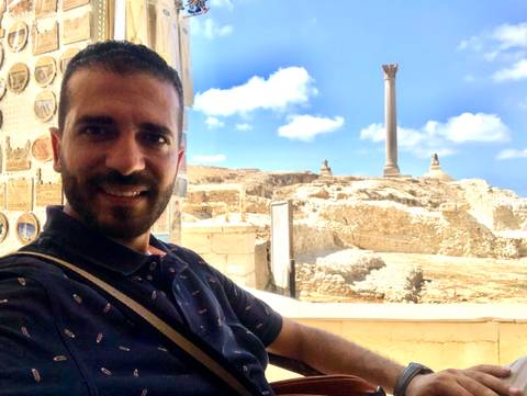 Smiling guide taking a selfie inside a cafe with Pompey’s Pillar visible outside