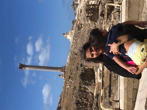 Mother holding child with Pompey’s Pillar towering behind under bright blue sky