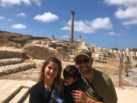 Smiling couple with sleepy child in front of ancient ruins and Pompey’s Pillar