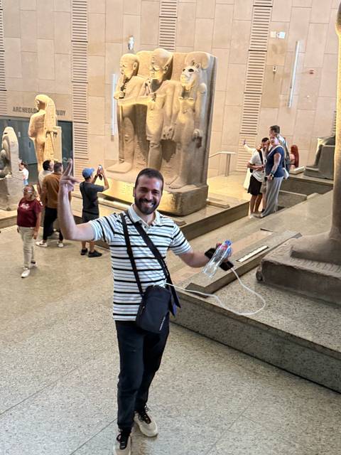 Tour guide celebrating inside the Egyptian Museum with statues and tourists around