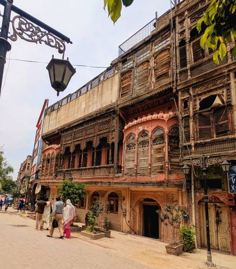 A weathered wooden merchant house with ornate balconies and carvings lines a historic street.
