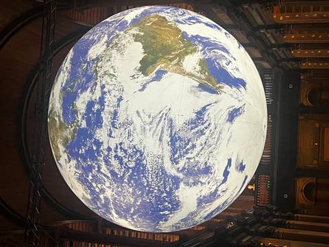 Giant illuminated globe art installation suspended inside a dark hall