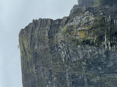 Tower-topped sea cliff with layers of grey rock and lichen seen on an overcast day