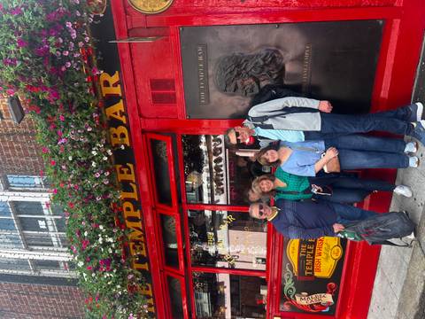 Four travellers smile in front of the bright red Temple Bar pub adorned with flowers in Dublin