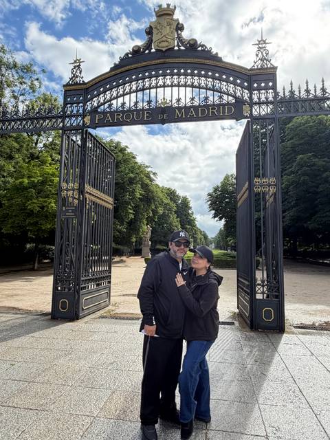 Couple embracing between ornate iron gates and tree-lined path on a cloudy day