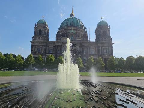 Berlin Cathedral fronted by a spraying fountain under clear sky.